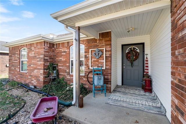 view of exterior entry featuring brick siding and covered porch