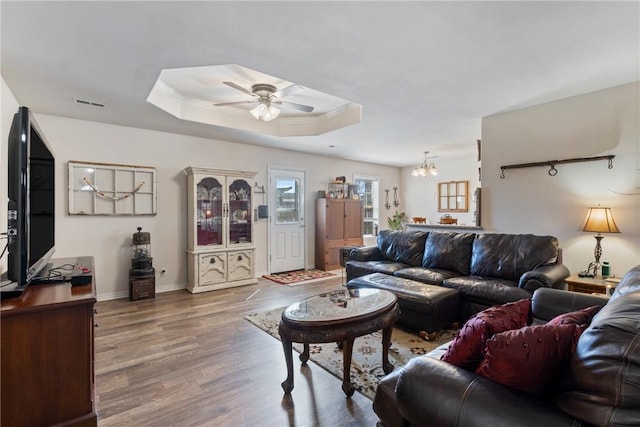 living room with visible vents, baseboards, ceiling fan with notable chandelier, wood finished floors, and a raised ceiling