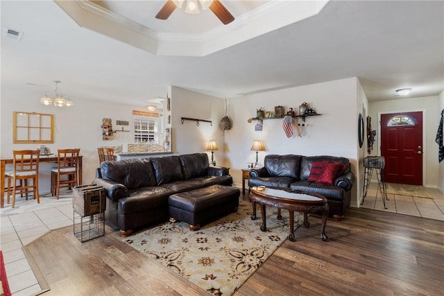 living area featuring visible vents, a tray ceiling, ornamental molding, ceiling fan with notable chandelier, and wood finished floors