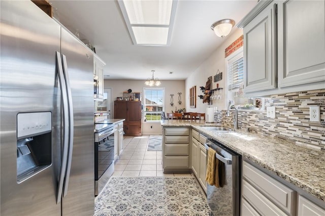 kitchen with light tile patterned floors, a peninsula, a sink, appliances with stainless steel finishes, and tasteful backsplash