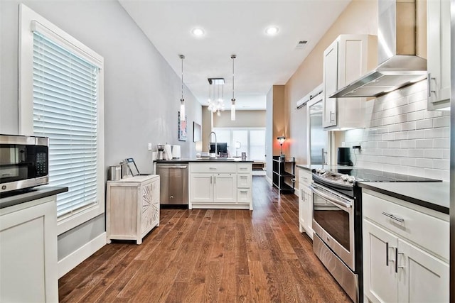 kitchen with dark wood finished floors, dark countertops, wall chimney exhaust hood, and appliances with stainless steel finishes
