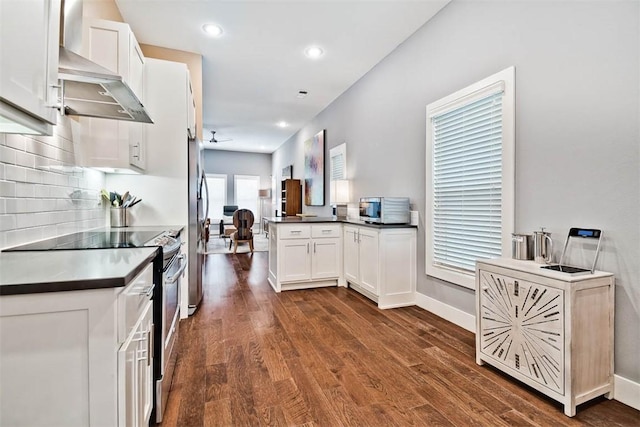 kitchen with backsplash, dark countertops, dark wood-style floors, appliances with stainless steel finishes, and wall chimney range hood