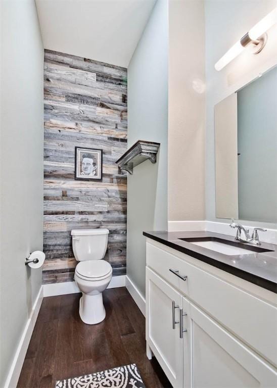 half bath with toilet, an accent wall, wood finished floors, baseboards, and vanity