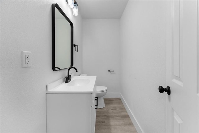 bathroom featuring baseboards, toilet, wood finished floors, and vanity