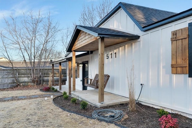 property entrance featuring board and batten siding, a shingled roof, and fence