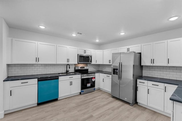 kitchen featuring light wood finished floors, visible vents, dark countertops, stainless steel appliances, and a sink