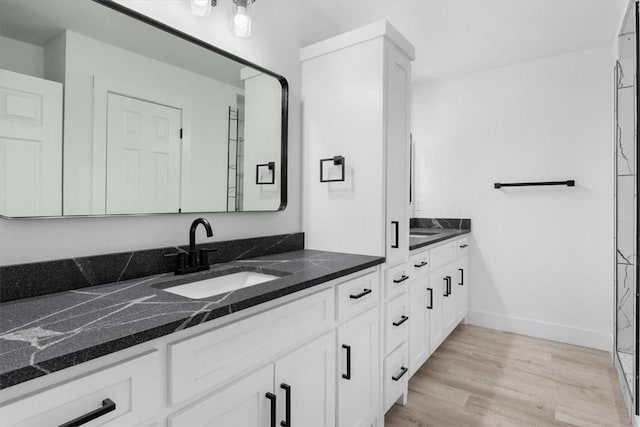 bathroom featuring double vanity, wood finished floors, baseboards, and a sink