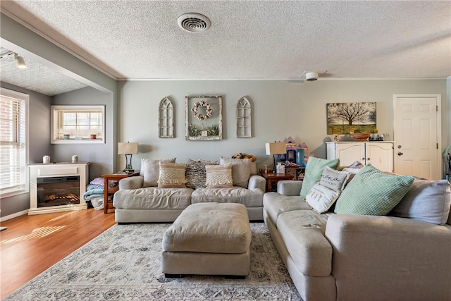 living room with visible vents, ornamental molding, a textured ceiling, and wood finished floors