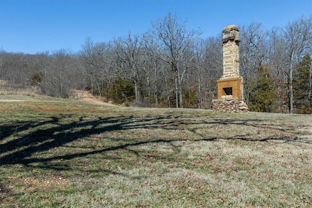 view of yard with exterior fireplace and a forest view