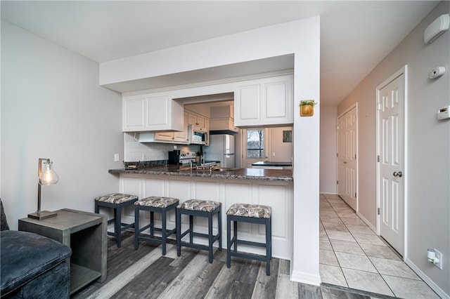 kitchen with tasteful backsplash, a kitchen breakfast bar, a peninsula, white appliances, and white cabinetry