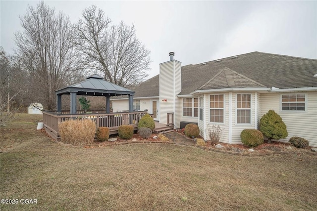 rear view of house with a lawn, a deck, a gazebo, a shingled roof, and a chimney