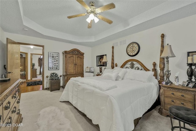 bedroom with a raised ceiling, light carpet, visible vents, and a textured ceiling