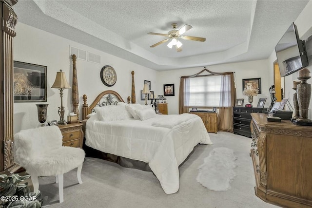 bedroom with visible vents, a ceiling fan, a textured ceiling, a raised ceiling, and light colored carpet