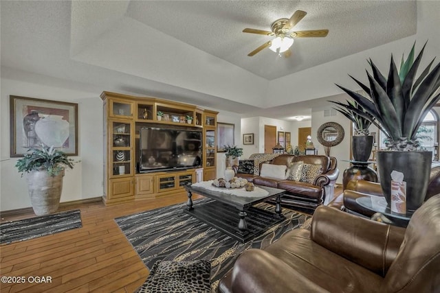 living area featuring a textured ceiling, light wood-type flooring, a raised ceiling, and a ceiling fan