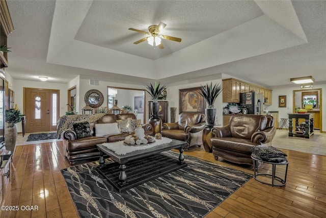 living area featuring a tray ceiling, a ceiling fan, light wood-type flooring, and a textured ceiling