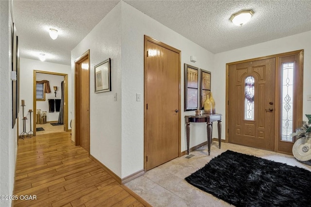 foyer featuring a textured wall, baseboards, a textured ceiling, and light wood finished floors