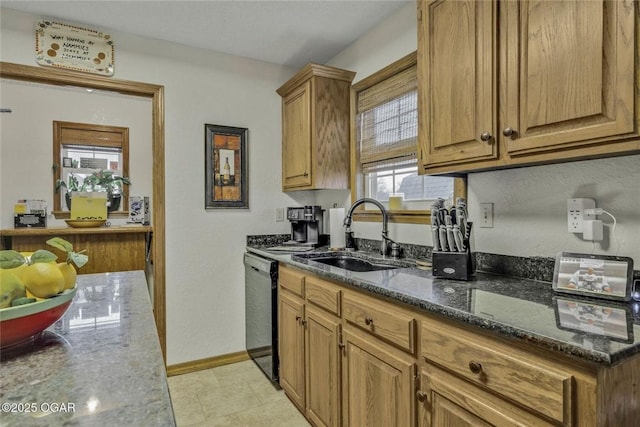 kitchen with baseboards, black dishwasher, dark stone countertops, brown cabinets, and a sink