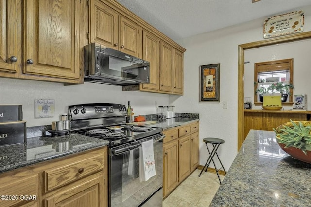 kitchen featuring black appliances, dark stone countertops, and brown cabinetry