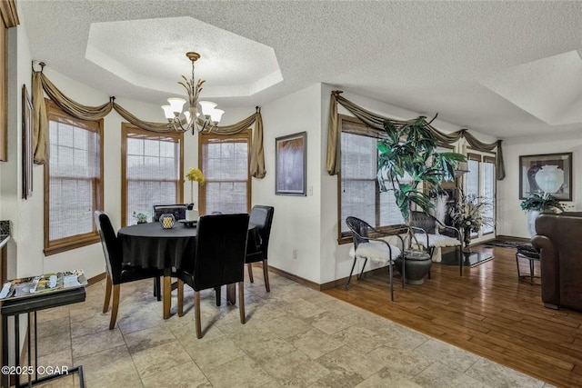 dining room with baseboards, a chandelier, light wood-type flooring, a tray ceiling, and a textured ceiling