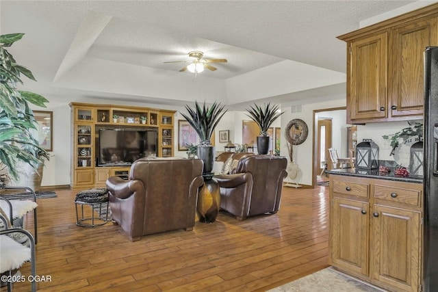 living area with hardwood / wood-style flooring, a ceiling fan, a raised ceiling, and a textured ceiling