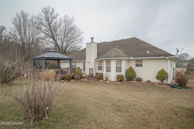 rear view of house featuring a lawn, a deck, a gazebo, a shingled roof, and a chimney