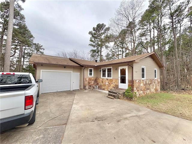 ranch-style home featuring concrete driveway, an attached garage, stone siding, and roof with shingles