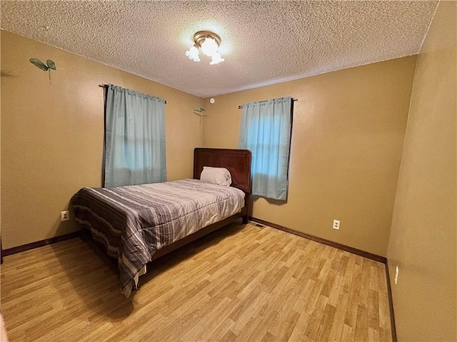 bedroom featuring light wood-style flooring, baseboards, and a textured ceiling