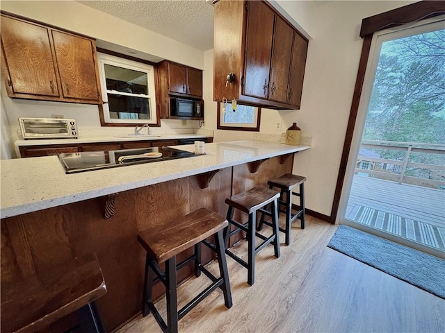 kitchen featuring black appliances, baseboards, light wood-style flooring, a kitchen breakfast bar, and a textured ceiling