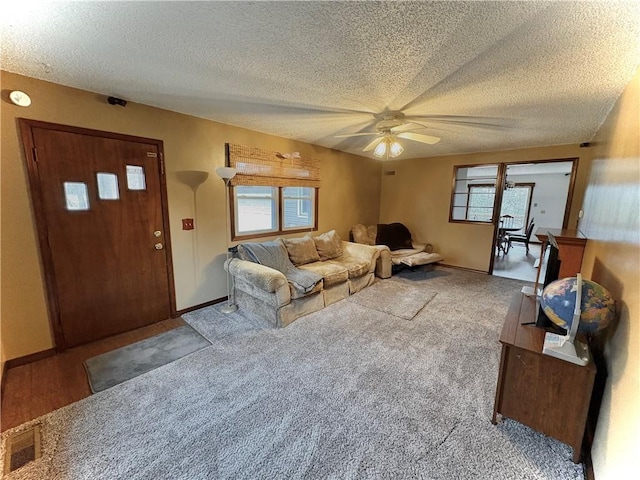 carpeted living room with visible vents, baseboards, a textured ceiling, and a ceiling fan