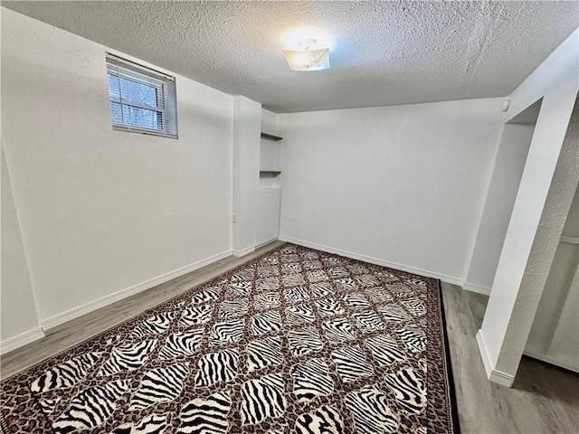 below grade area with wood finished floors, baseboards, and a textured ceiling