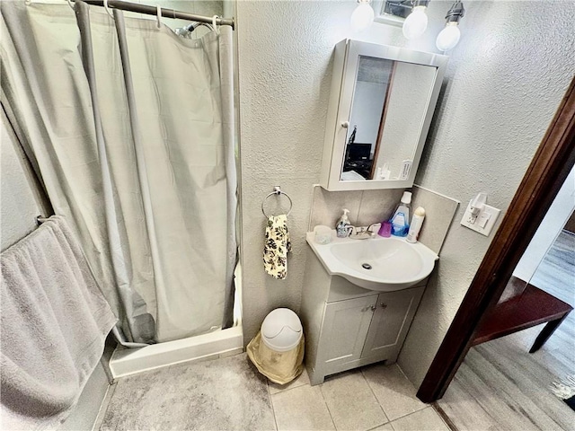 full bath featuring vanity, a textured wall, a stall shower, and tile patterned flooring