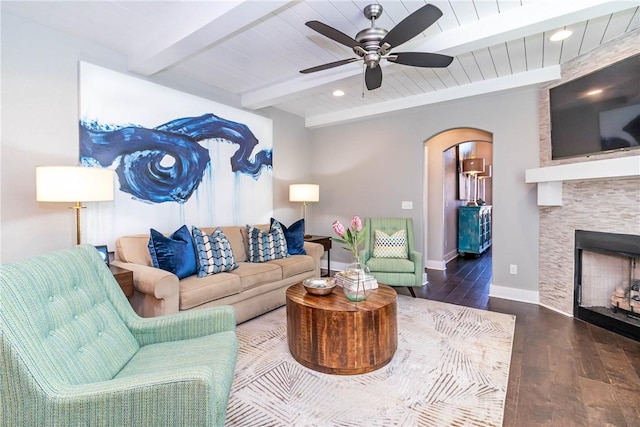 living area with wood finished floors, baseboards, beam ceiling, arched walkways, and ceiling fan