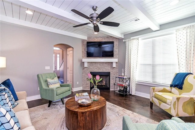 living room with baseboards, beam ceiling, a fireplace, arched walkways, and a ceiling fan