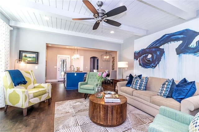 living area featuring dark wood finished floors, beamed ceiling, wooden ceiling, arched walkways, and a ceiling fan