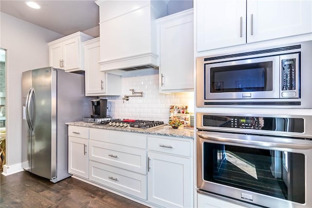 kitchen with light stone counters, tasteful backsplash, stainless steel appliances, white cabinets, and custom exhaust hood