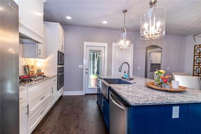 kitchen with a center island with sink, arched walkways, a sink, appliances with stainless steel finishes, and a notable chandelier