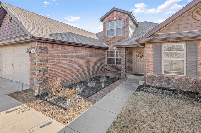 entrance to property featuring an attached garage, brick siding, and roof with shingles