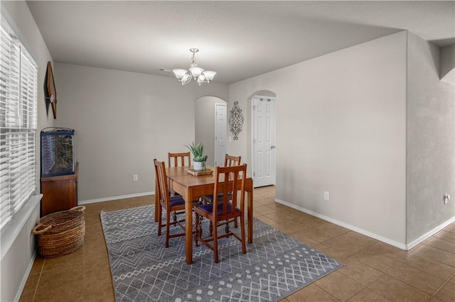 tiled dining room with baseboards, arched walkways, and a chandelier