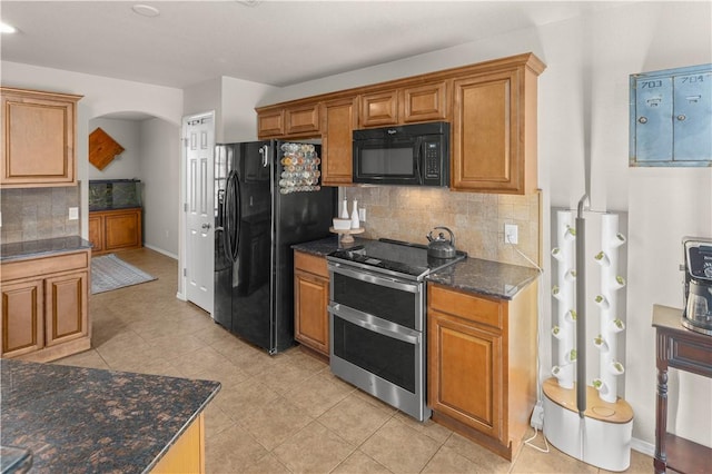 kitchen with backsplash, brown cabinetry, dark stone countertops, arched walkways, and black appliances