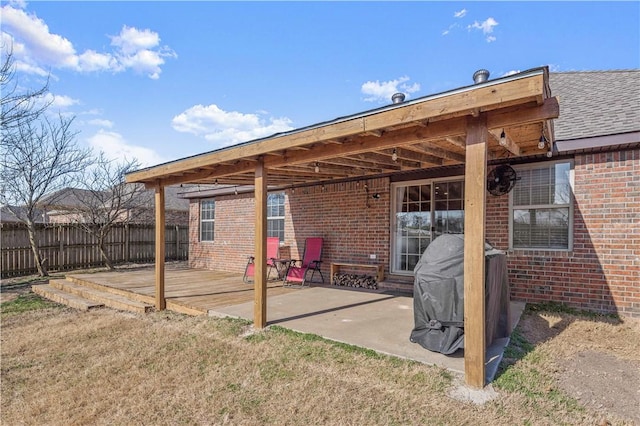 rear view of house featuring a deck, a patio, fence, and brick siding