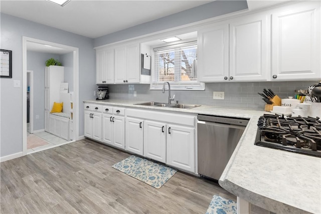 kitchen with light wood finished floors, light countertops, stainless steel dishwasher, white cabinets, and a sink