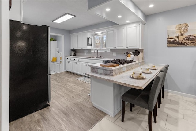 kitchen featuring a sink, appliances with stainless steel finishes, a peninsula, white cabinets, and light countertops