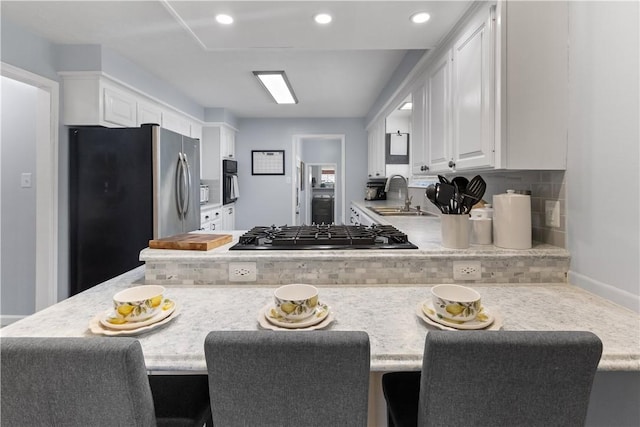 kitchen with stainless steel fridge, white cabinetry, black gas stovetop, and a sink