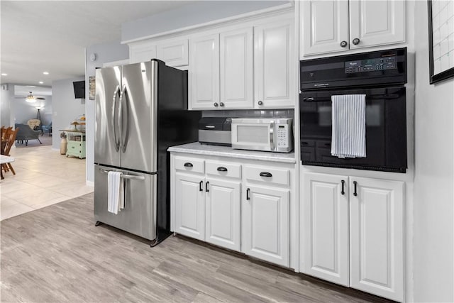 kitchen with white microwave, freestanding refrigerator, ceiling fan, white cabinets, and black oven