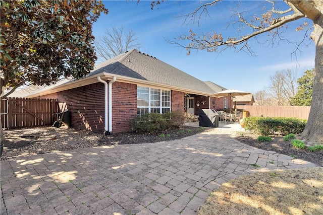 rear view of property with fence, a patio area, brick siding, and a shingled roof