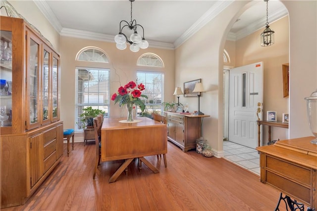 foyer entrance with arched walkways, light wood-type flooring, an inviting chandelier, and ornamental molding