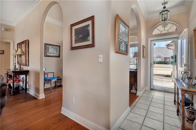 foyer with crown molding, light wood-style flooring, baseboards, and arched walkways