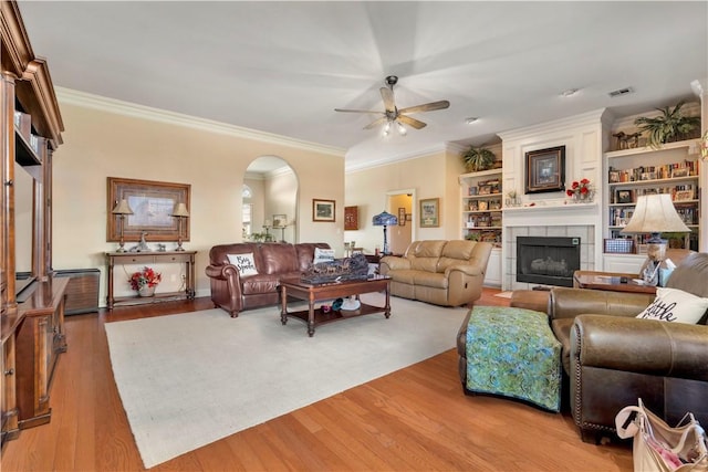 living room with light wood-type flooring, visible vents, a ceiling fan, arched walkways, and a fireplace