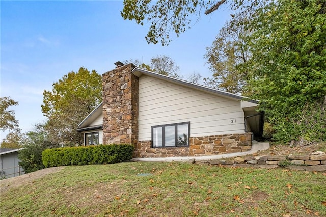 view of home's exterior with a yard, stone siding, and a chimney