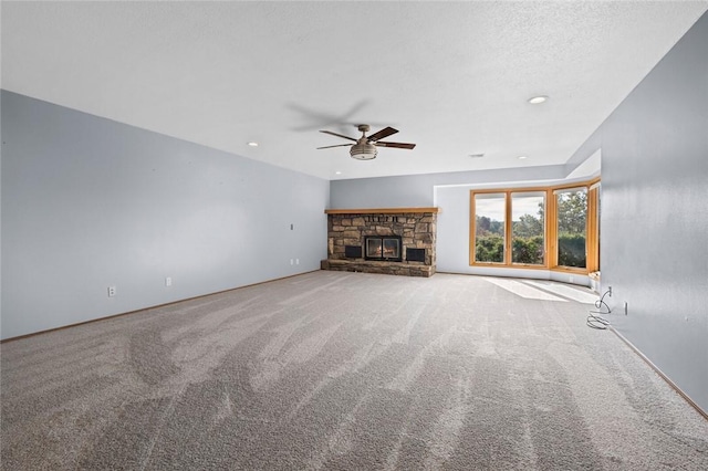 unfurnished living room with a stone fireplace, carpet flooring, a ceiling fan, and a textured ceiling